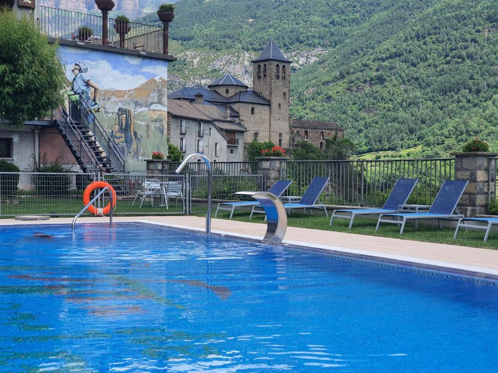 a swimming pool with blue chairs and a castle at Hotel Villa de Torla in Torla-Ordesa