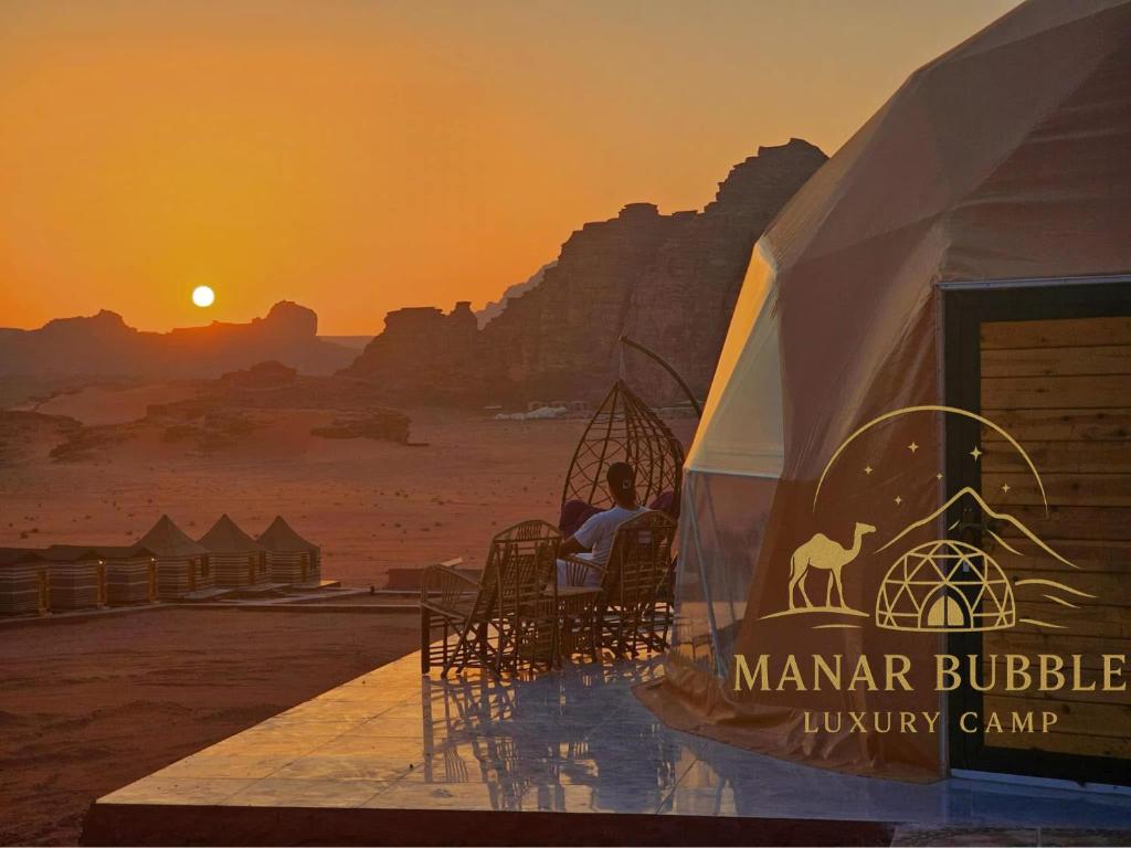 a man sitting in a chair in a tent with the sunset at Manar Bubble Luxury Camp in Wadi Rum