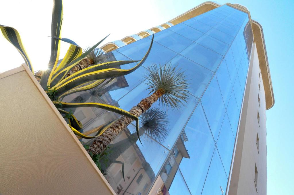 a tall glass building with a palm tree in front of it at Suite & Spa Mirabel in Grado