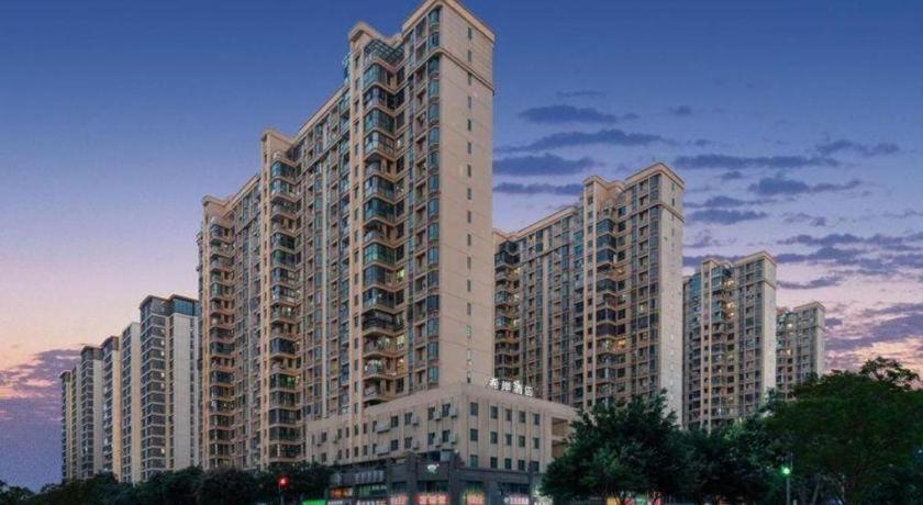 a large apartment building with a sunset in the background at Xana Hotelle Xiamen Airport Zone Government in Xiamen