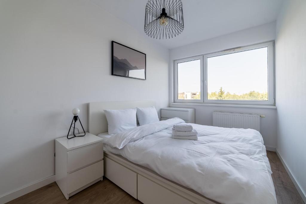 a white bedroom with a bed and a window at Osiedle Szafirowe Chic Apartment by BookingHost in Suchy Las