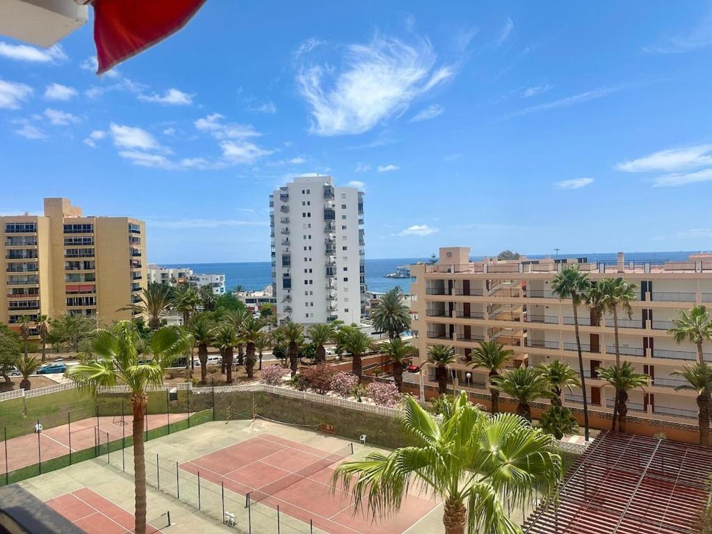 a view of a tennis court with palm trees and buildings at Seaside Two Bedroom Apartment in Los Cristianos