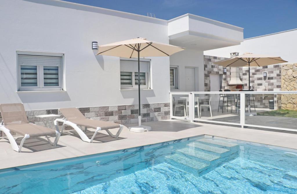 a swimming pool with two chairs and an umbrella at El Rincon de Samuel in Conil de la Frontera