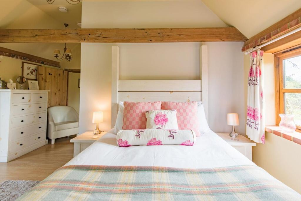 a bedroom with a large bed with pink pillows at Pond Cottage by Keepers Cottages in Egerton