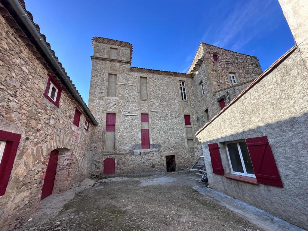 - un grand bâtiment en pierre avec des portes et des fenêtres rouges dans l'établissement La Maison du Figuier, à Cournanel