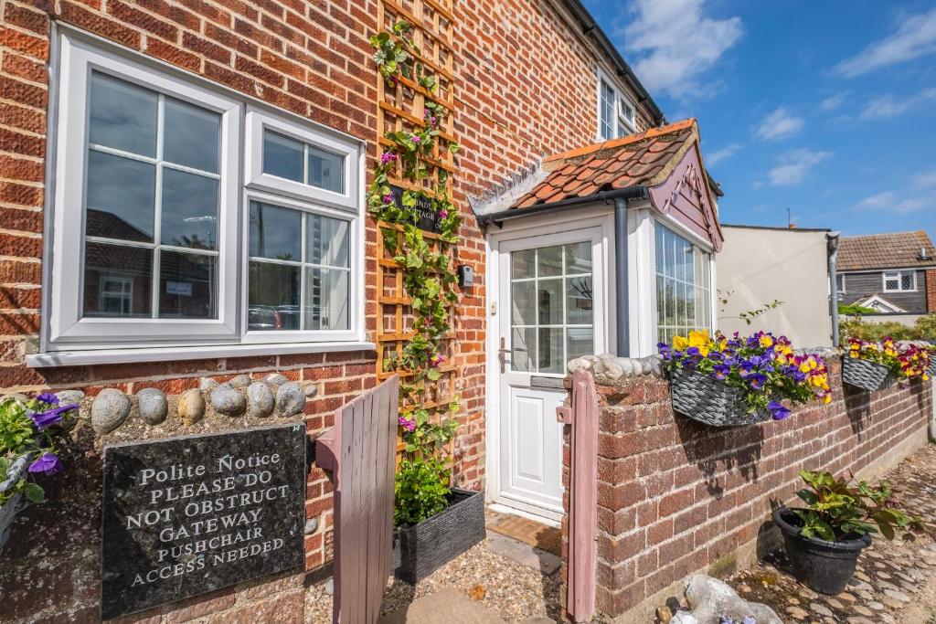 une maison en briques avec un panneau devant elle dans l'établissement Winterton Sea Sanctuary, Hot Tub & Log Burner by the Dunes, à Winterton-on-Sea