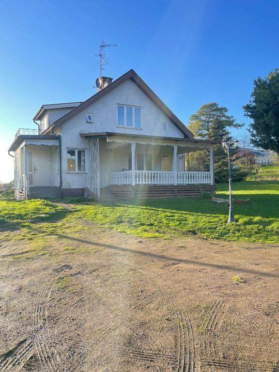 a white house with a porch on a dirt road at Hus på bondgård in Gunnarskog