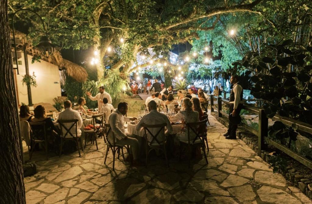 a group of people sitting at tables in a garden at night at River Glamping Boutique Jarabacoa in Jarabacoa