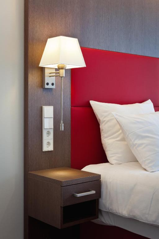 a bed with a red headboard and a table with a lamp at Mondorf Parc Hotel & Spa in Mondorf-les-Bains