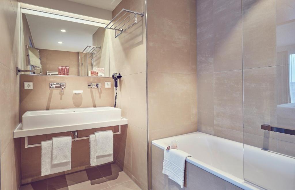 a bathroom with a sink and a tub and a shower at Mondorf Parc Hotel & Spa in Mondorf-les-Bains
