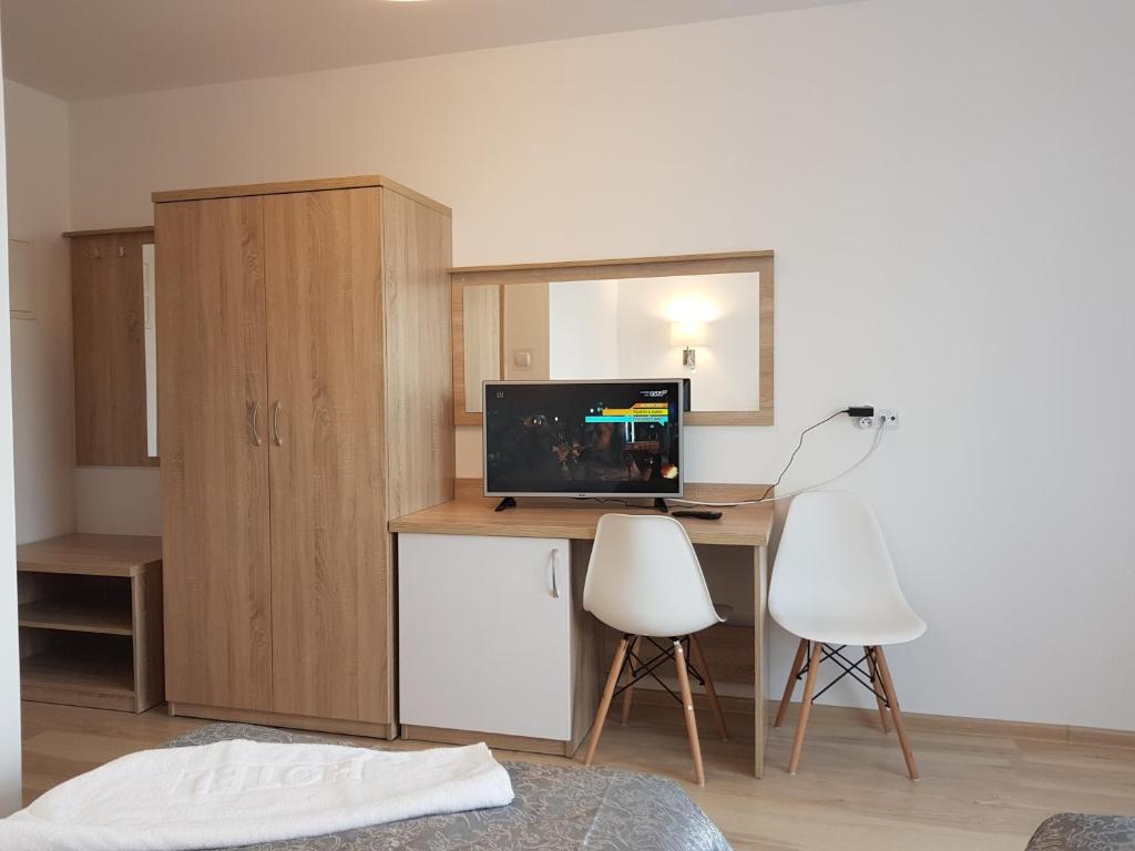 Hotel room with wooden furniture, TV, and two chairs.
