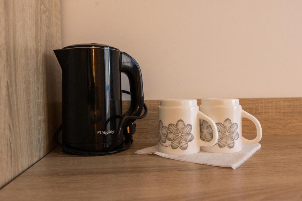 Black electric kettle and two floral mugs on a wooden surface.
