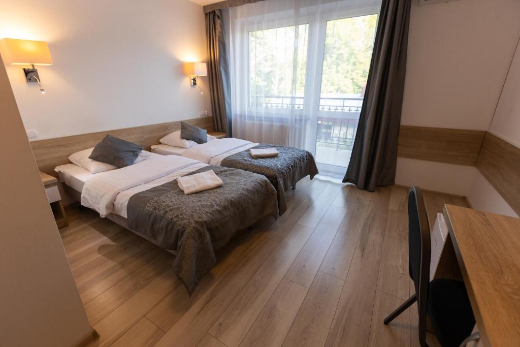 Cozy hotel room with twin beds, wooden floor, and large window.