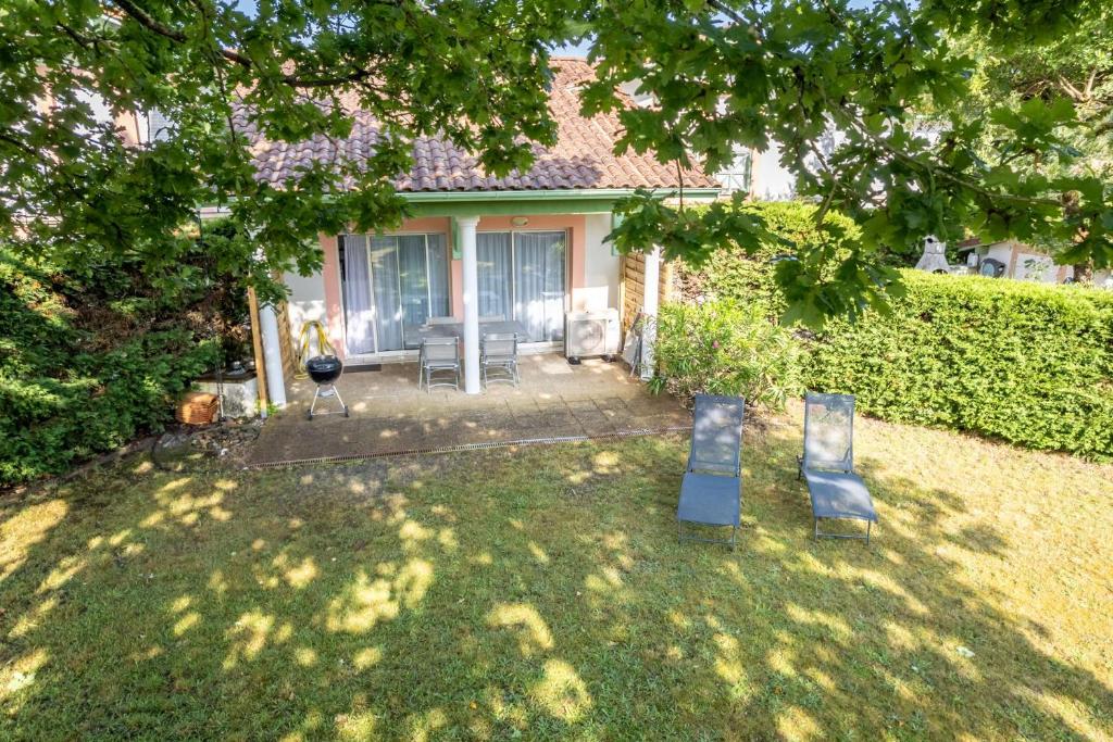 a yard with two chairs in front of a house at Proche lac : Maison avec beau jardin in Biscarrosse