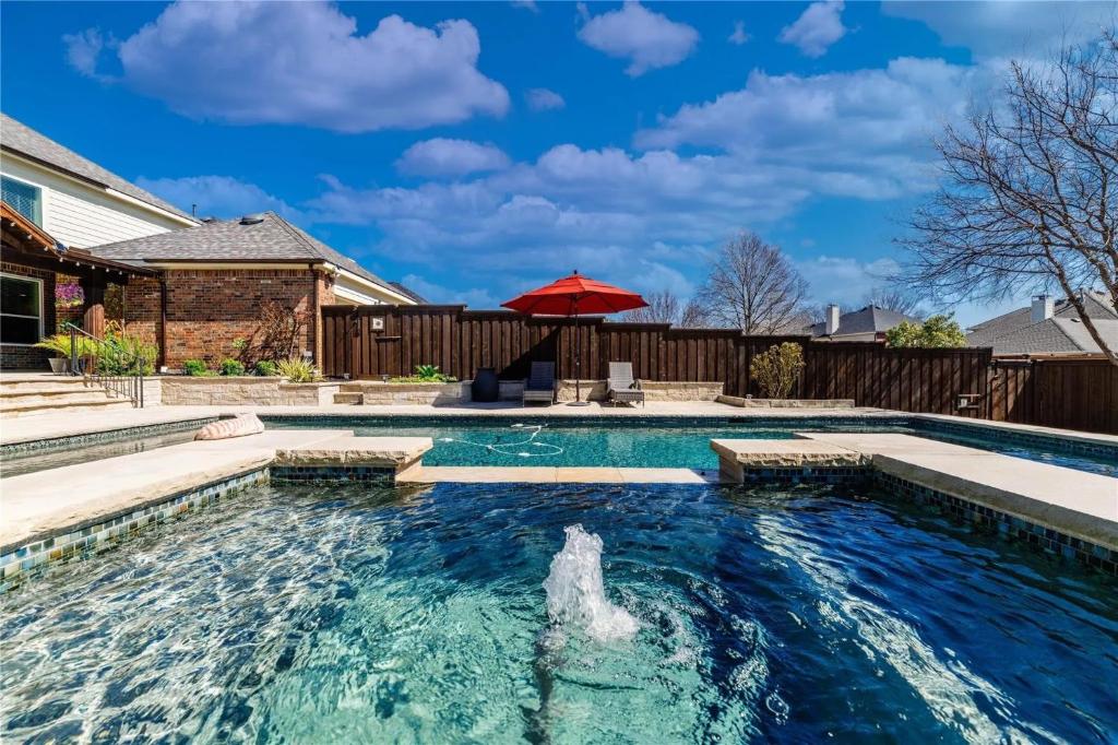 a swimming pool with a red umbrella in a backyard at The Sapphire Sanctuary with Pool in Allen