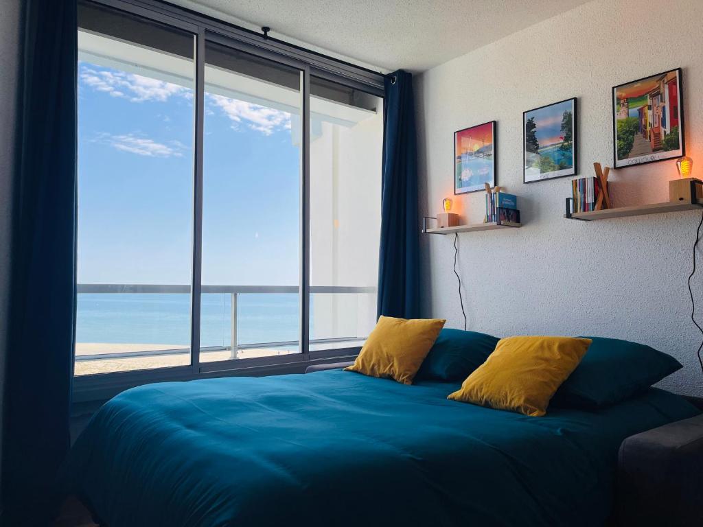 une chambre avec un lit bleu et une grande fenêtre dans l'établissement Evasion en Bord de Mer, au Barcarès