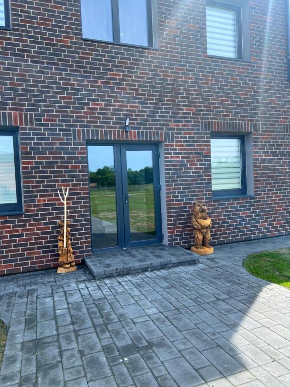 a brick building with a glass door and two statues at Svečių namai PAS MEŠKĄ in Karklė