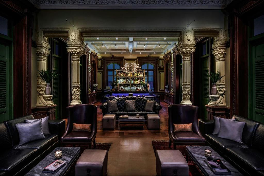 An ornate lounge with leather sofas, armchairs and a chandelier-lit bar beyond.