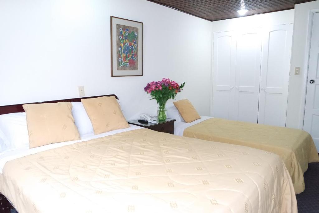 twee bedden in een kamer met een vaas met bloemen bij Hotel Casa Rincón del Chicó in Bogota