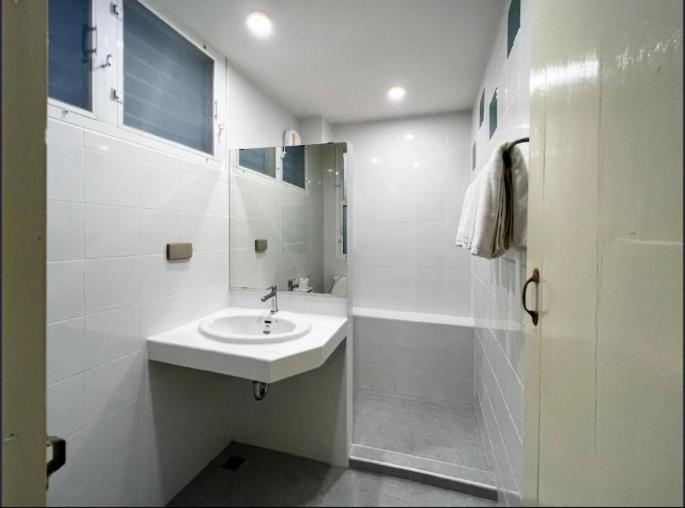 a white bathroom with a sink and a shower at Niagara Hotel in Bangkok