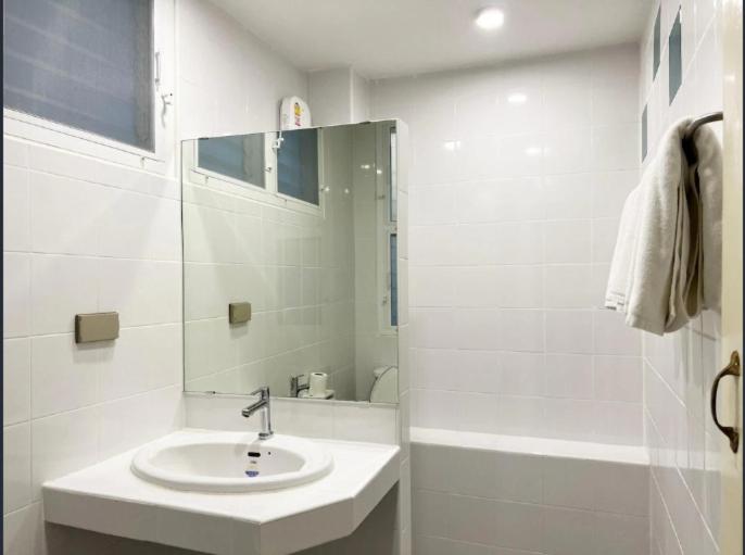 a white bathroom with a sink and a mirror at Niagara Hotel in Bangkok