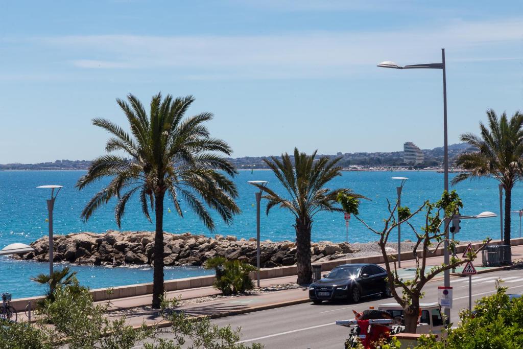 Une voiture qui descend sur une route avec des palmiers et l'océan dans l'établissement La Maison Du Pêcheur, à Cagnes-sur-Mer