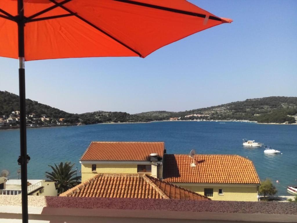 a red umbrella in front of a house with the water at Apartments Perina in Tisno