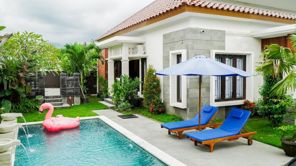 a pool with two chairs and an umbrella next to a house at Puri Anturan Lovina in Lovina