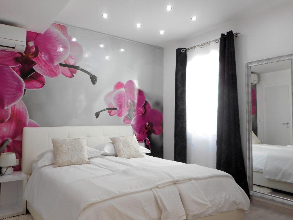 1 dormitorio con 1 cama blanca con orquídeas rosas en la pared en Palladium City Center Apartments, en Makarska