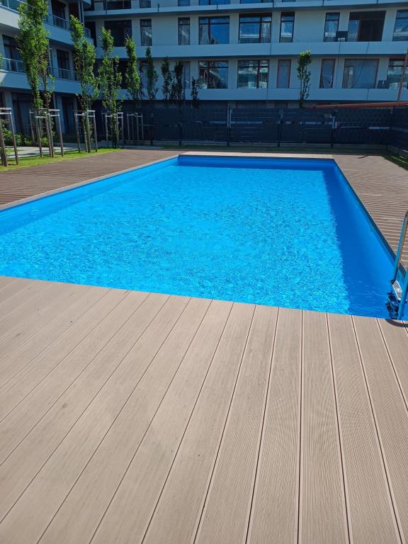 a blue swimming pool with a wooden floor and a building at Apartament rodzinny 47, 150 m od plaży, basen, plac zabaw, darmowy parking! in Sianozety