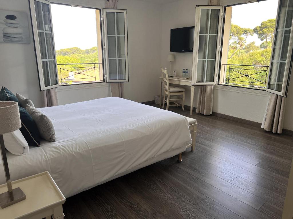 a bedroom with a bed and two windows and a desk at Hôtel Beau Site - Cap d'Antibes in Antibes