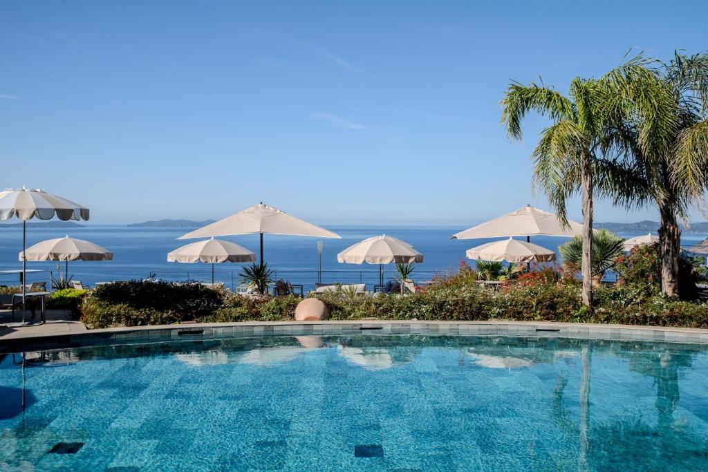a swimming pool with umbrellas and the ocean at Hôtel La Villa Douce in Rayol-Canadel-sur-Mer
