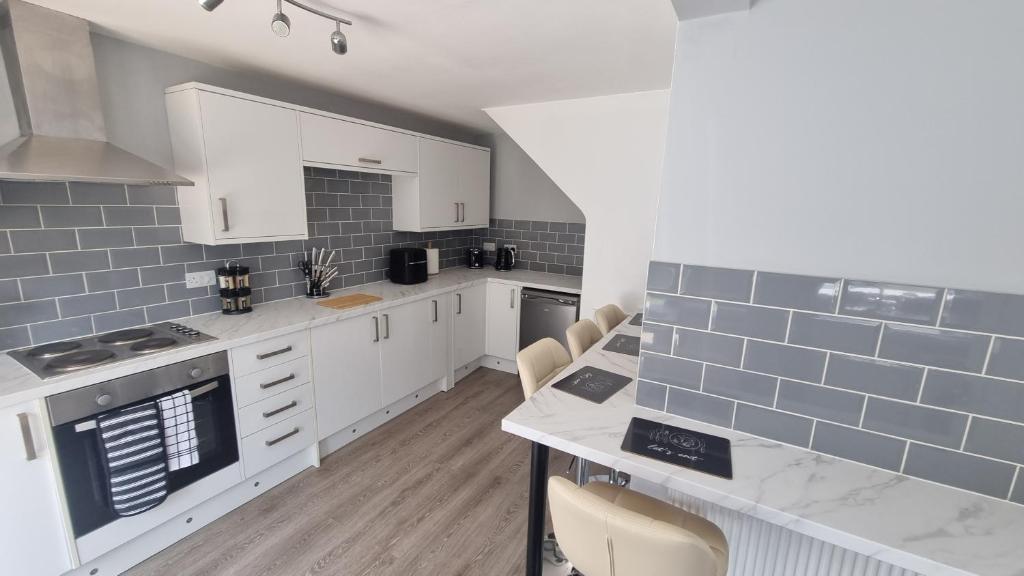 a kitchen with white cabinets and blue tiles on the wall at Spencer , 4 bed slp 8 semi in Lee On The Solent in Lee-on-the-Solent