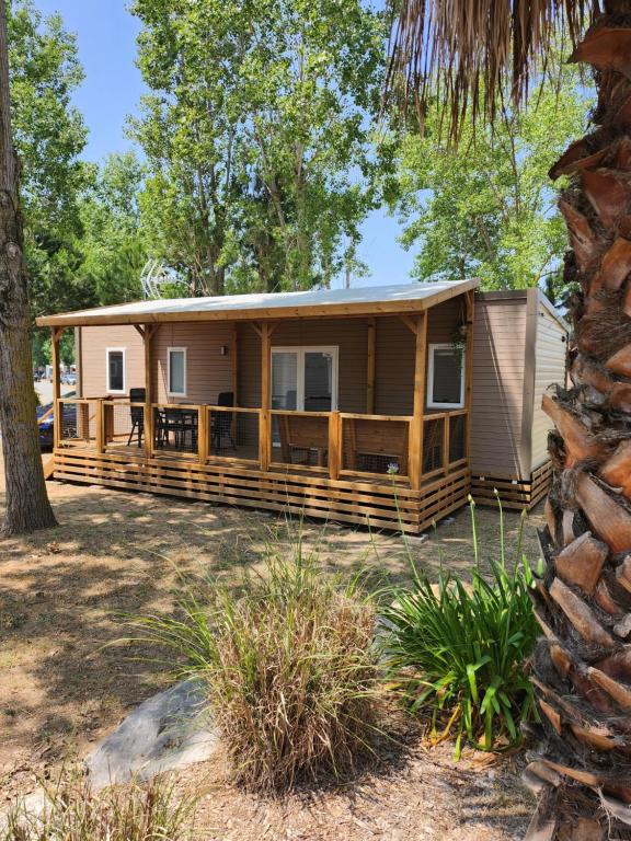 a house with a wrap around porch with a tree at Mobil home luxe 3 ch dont une suite parentale clim terrasse bois couverte La Yole 5 étoiles in Vendres