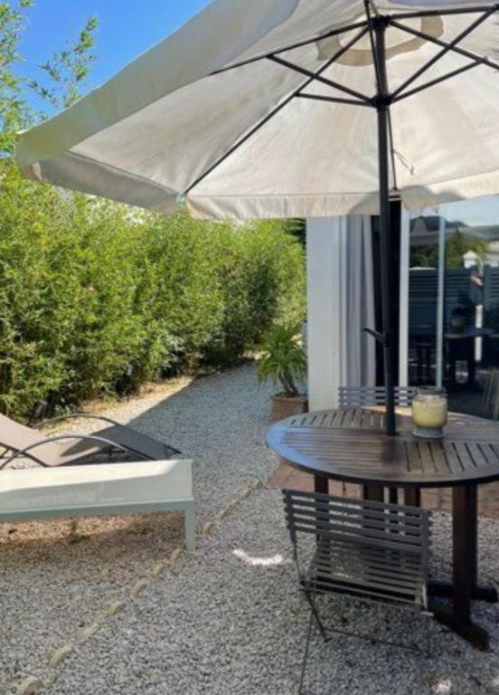une table en bois avec un parasol à côté d'un banc dans l'établissement Maisonette L'OLIVIER, à Pérols