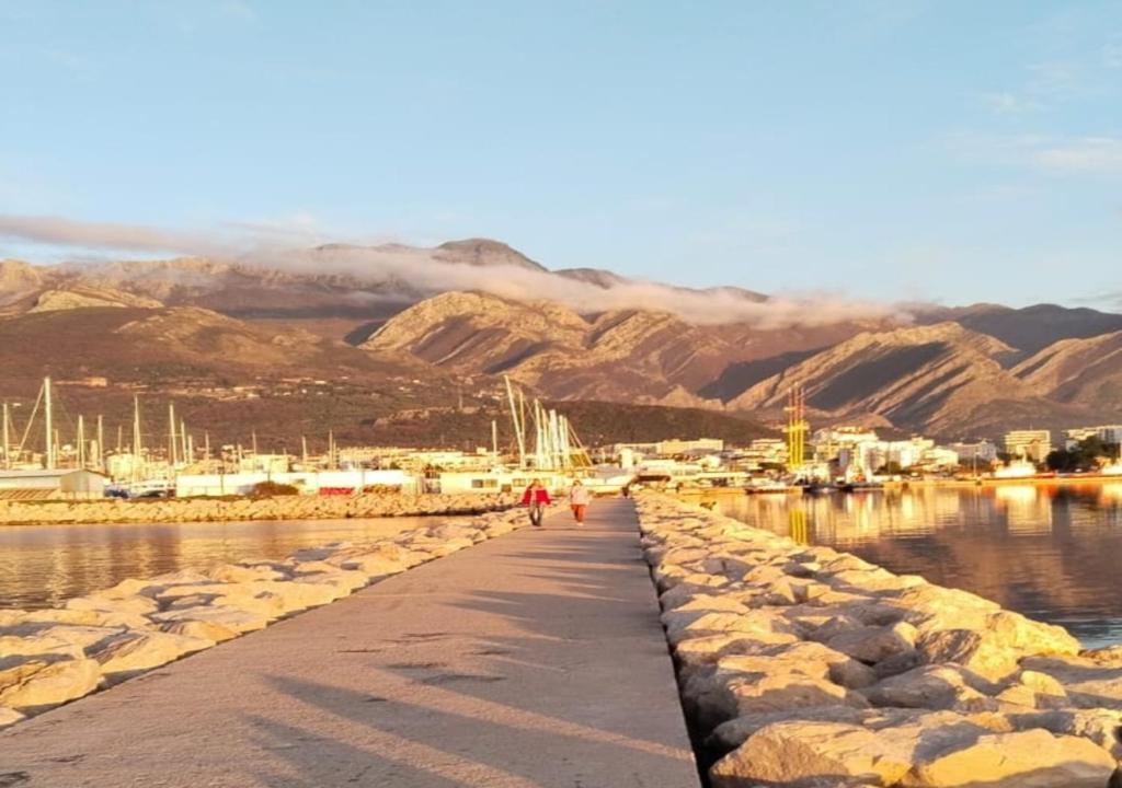 Una pasarela que conduce a un puerto deportivo con montañas al fondo. en Apartmani Kolovic Susanj, en Bar