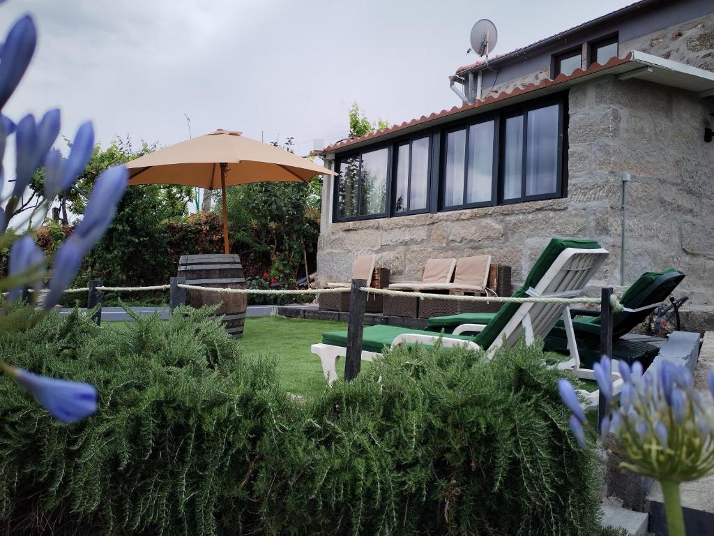 a house with two lawn chairs and an umbrella at Belo Encanto do Paiva in Castelo de Paiva