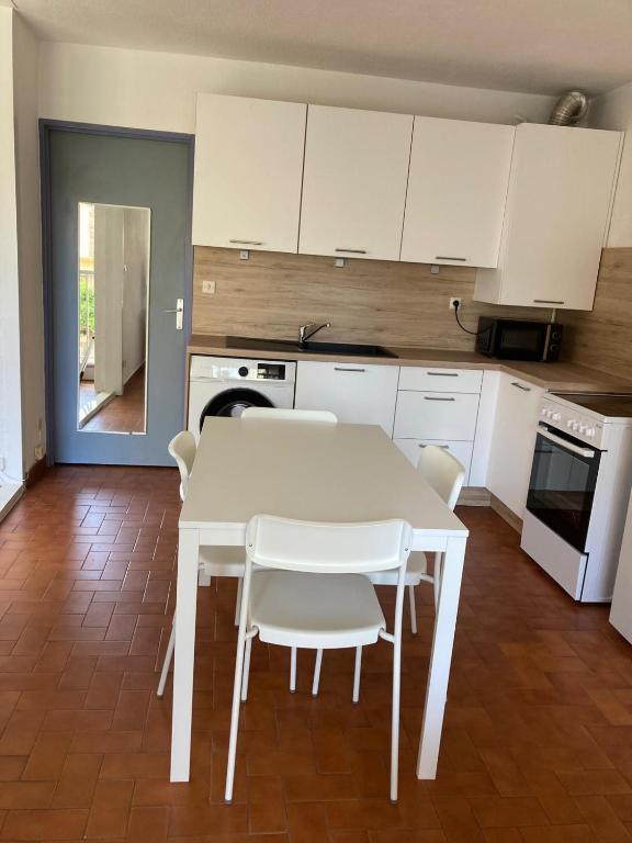 - une cuisine avec une table blanche et des chaises blanches dans l'établissement Grand T2 à Gruissan, calme, vue sur le port, à Gruissan