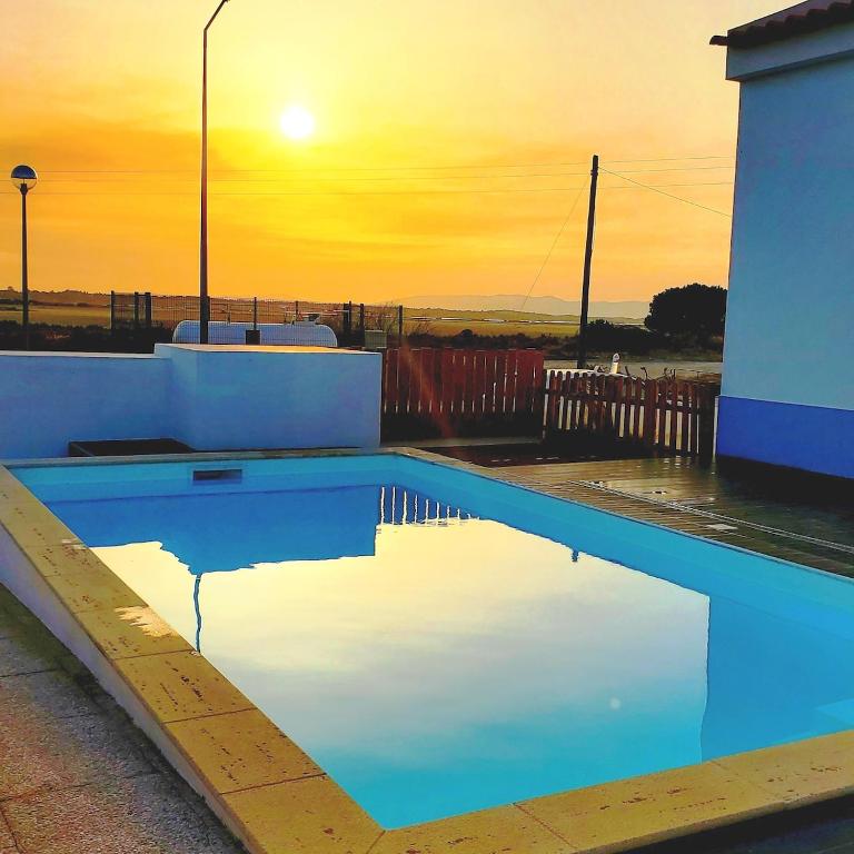 a swimming pool with a sunset in the background at Maison de Sable - Possanco in Comporta
