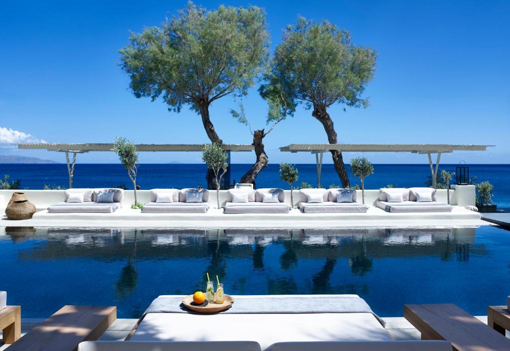 een zwembad met witte banken en bomen en de oceaan bij Bellonias Villas in Kamari