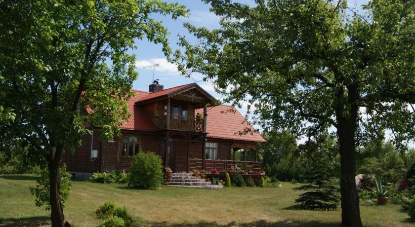 a wooden house with a red roof on a field at Kurpiowska Chatka in Stanisławowo