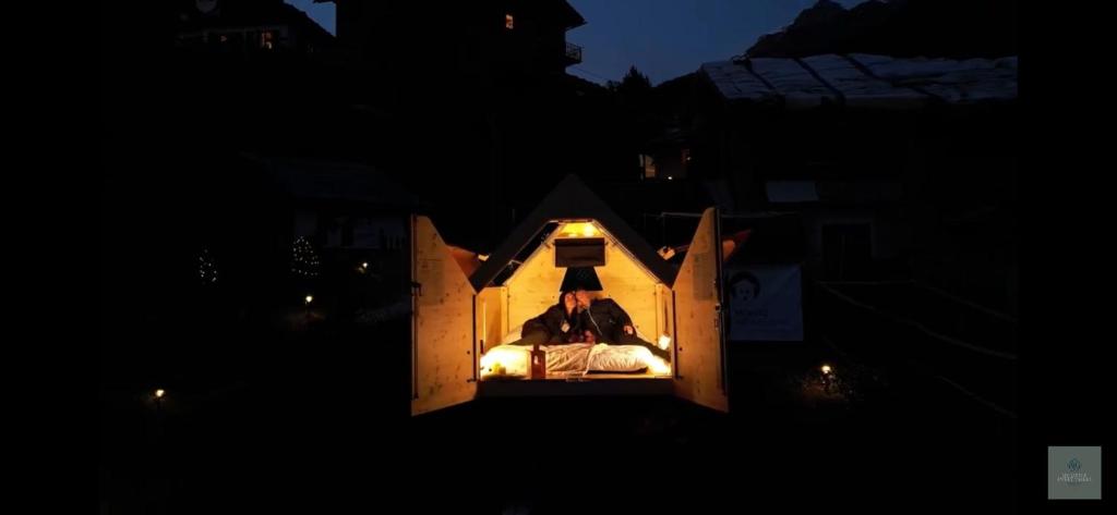 a man sitting in a dog house at night at Starsbox e romantica camera in Valtournenche