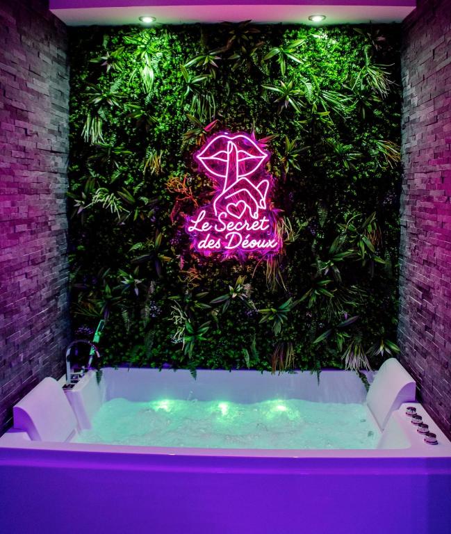 un mur végétal derrière une baignoire avec une enseigne au néon dans l'établissement Le secret des déoux love room, à Forcalqueiret