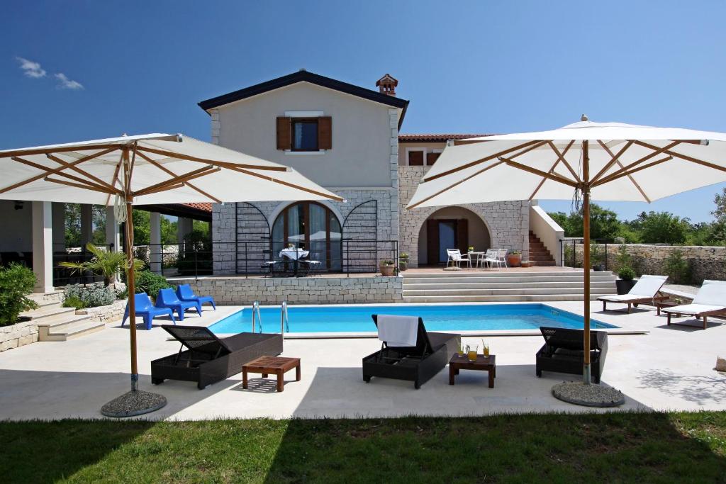 a swimming pool with two umbrellas and chairs next to a house at Villa Histra in Čabrunići