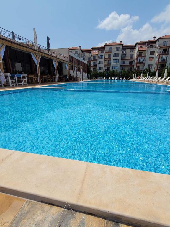 a large blue swimming pool with chairs and buildings at Famagusta Antoniya in Aheloy