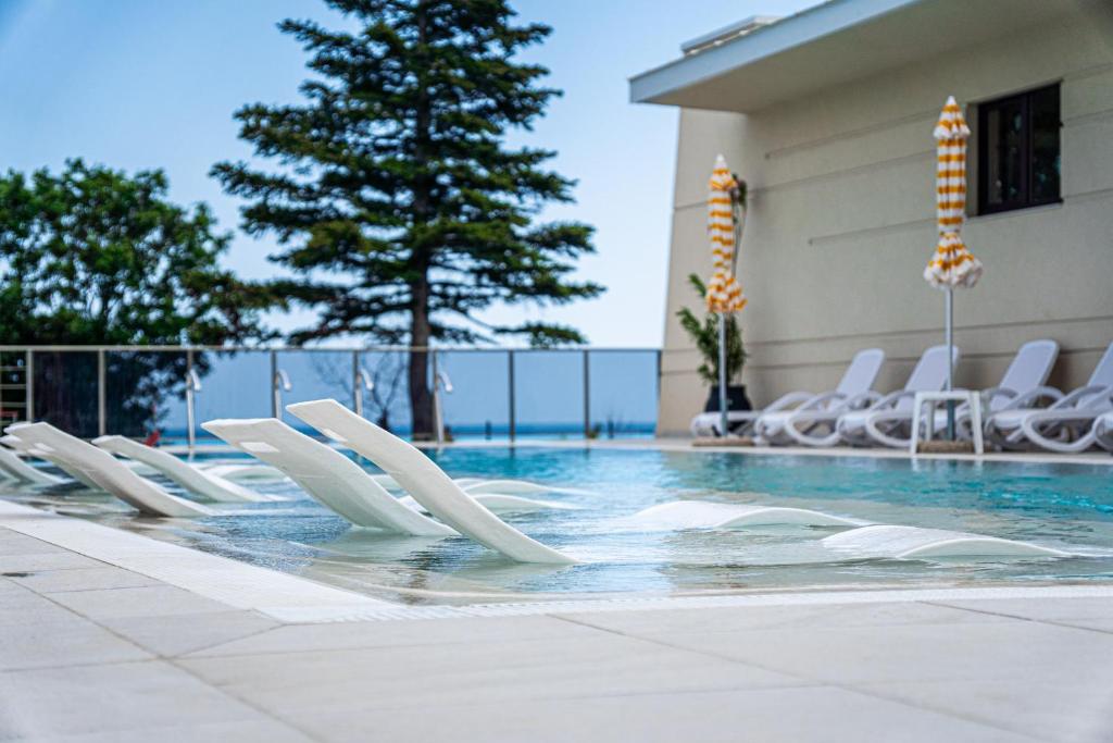 a swimming pool with white chairs and a tree at Skyline 11B Apartment - Sea View,Pools & SPA in Varna City