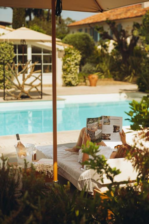 a person laying on a chaise lounge reading a book next to a pool at La Bastide des Salins in Saint-Tropez