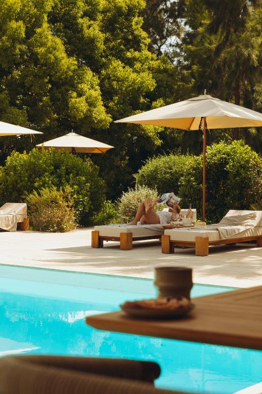 a woman laying on beds next to a pool with an umbrella at La Bastide des Salins in Saint-Tropez