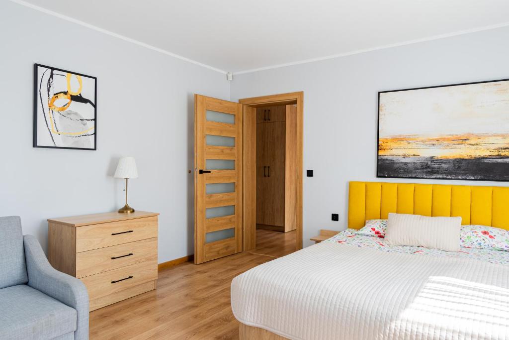 a white bedroom with a bed and a chair at Fajne Apartamenty - Karwia - Blisko Plaży - Komfort i Cisza in Karwia