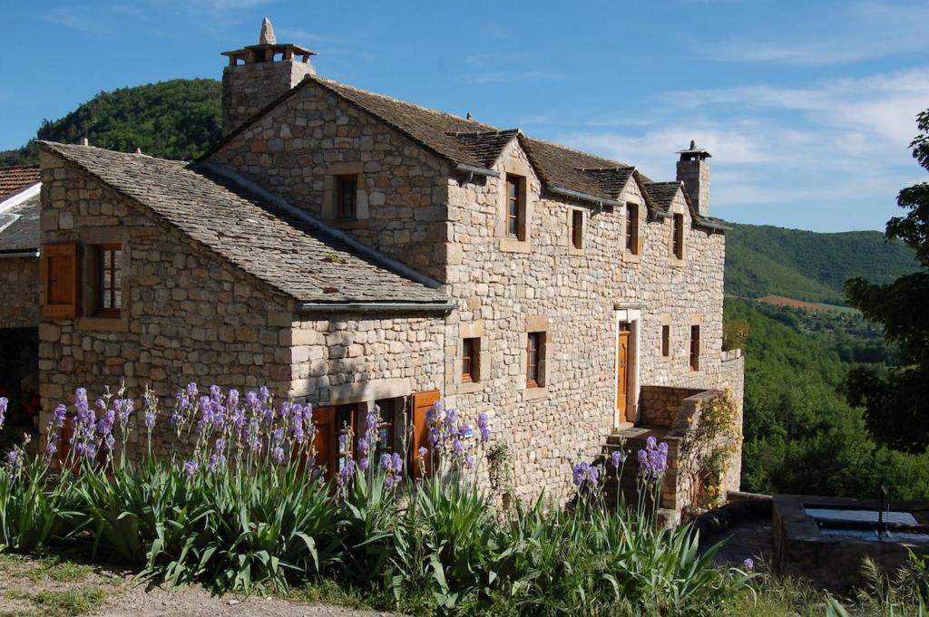 une ancienne maison en pierre avec des fleurs violettes devant elle dans l'établissement Gîte Lou Clapas dans village perché du Parc des Grands Causses, à Nant